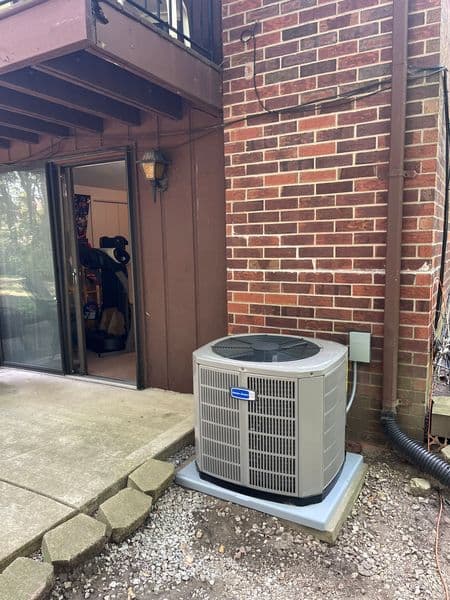 Air conditioning unit installed outside a brick building, near a patio area.