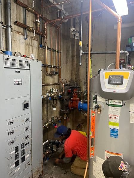 Plumber working on pipes and water heater in a commercial maintenance room.