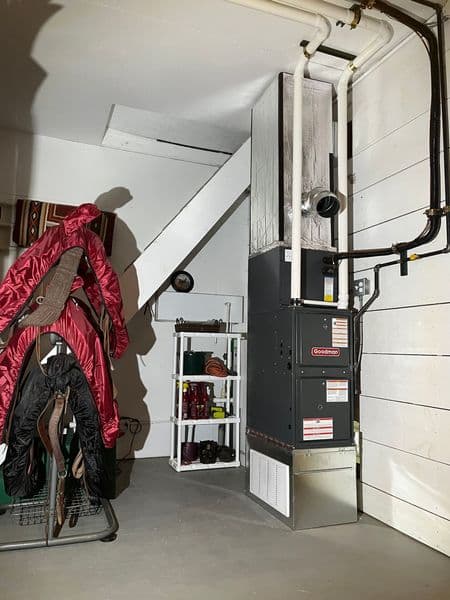Furnace in a basement with coats on a rack and storage shelves nearby.