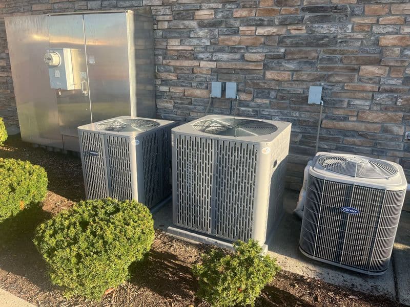 Air conditioning units beside a stone wall, with a meter box and landscaping shrubs.