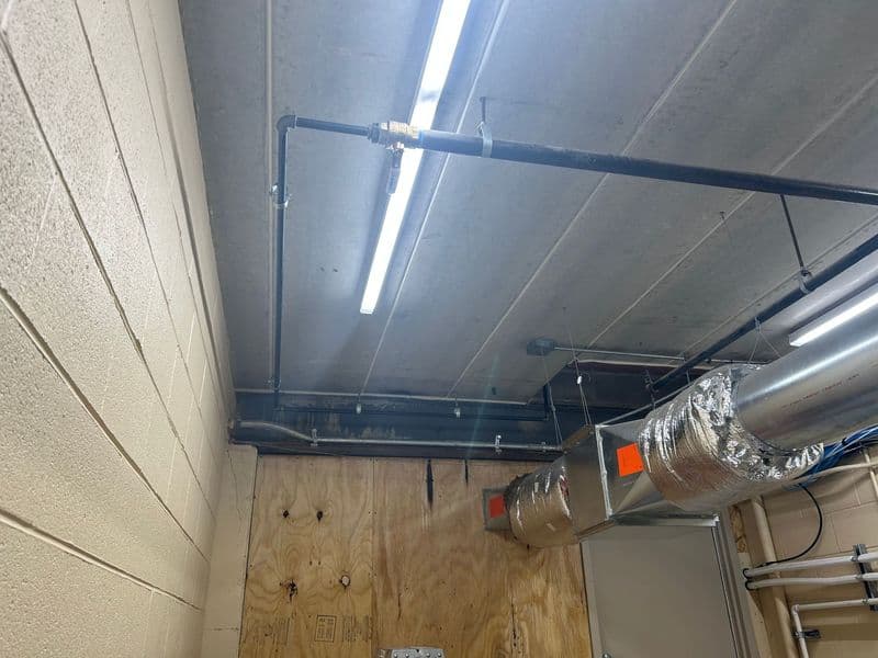 Ceiling view showing ventilation ductwork and fluorescent lighting in a utility room.