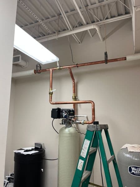 Copper plumbing installation with water filtration system, ladder, and workspace background.
