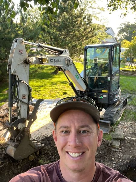 Man taking a selfie with a Bobcat excavator in a green outdoor setting.