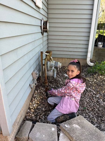 Young girl in a pink jacket checking a water meter outside a house.