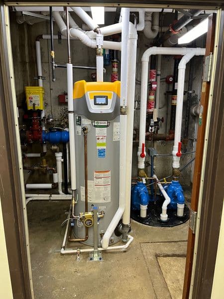 Modern water heater installation with plumbing pipes in a utility room.