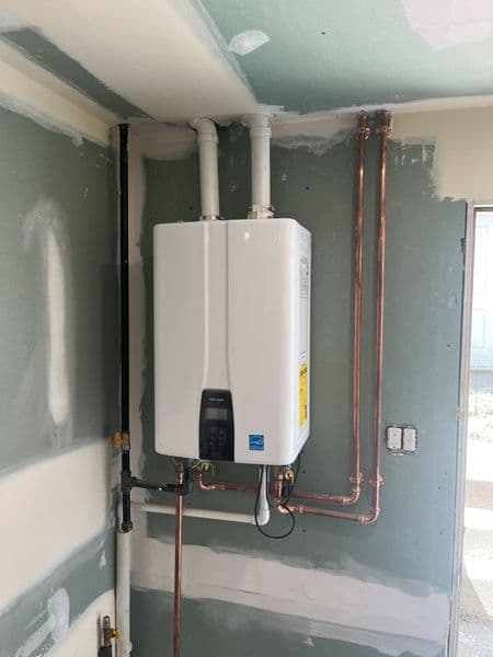 Tankless water heater installation in a partially finished wall with copper piping.