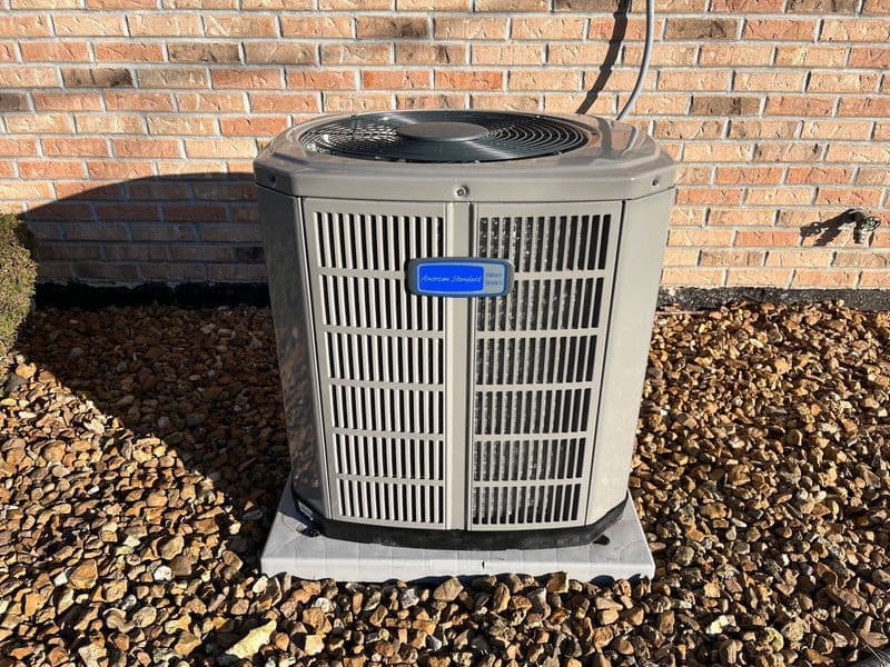 New air conditioning unit installed outside against a brick wall with gravel landscaping.