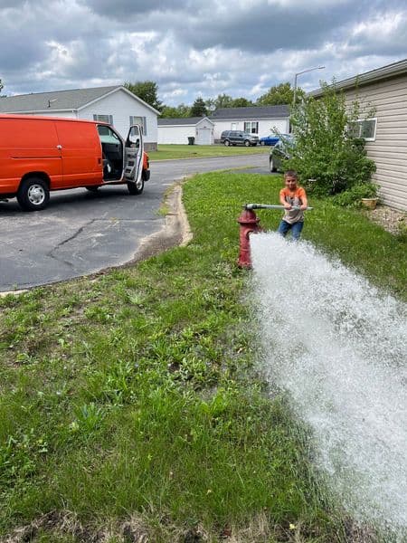 Child playing with water from a fire hydrant in a residential area with a van nearby.