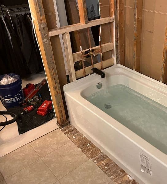 Newly installed bathtub with water, surrounded by unfinished walls and construction tools.