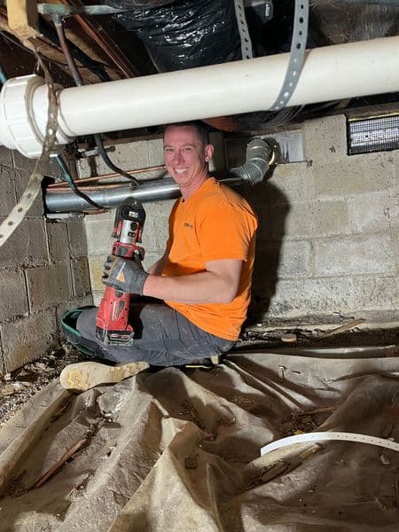 Man in an orange shirt using a power tool in a basement renovation project.