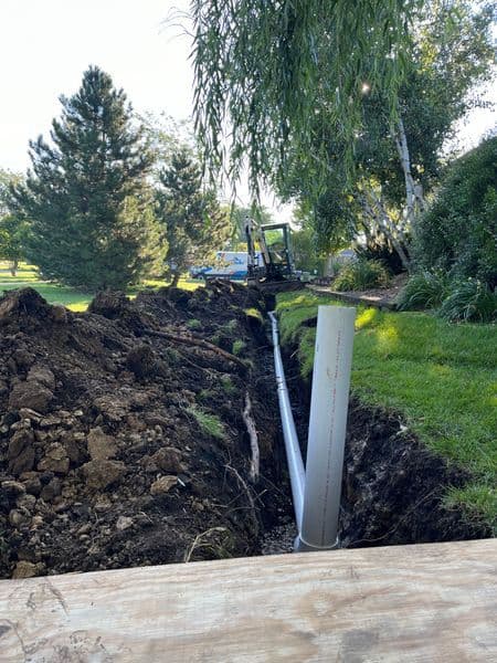 Excavation site with a trench for piping installation surrounded by greenery.