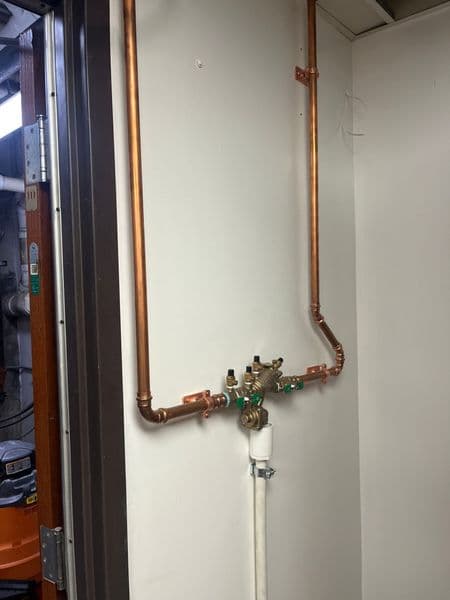 Copper plumbing installation with valves and fittings against a neutral wall.