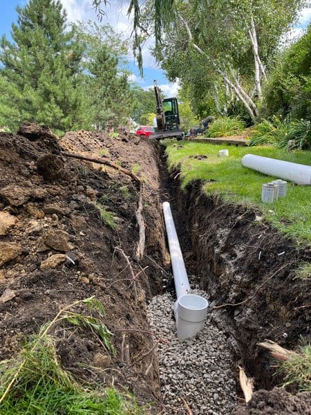 Excavated trench for drainage installation with gravel and large pipe in residential yard.