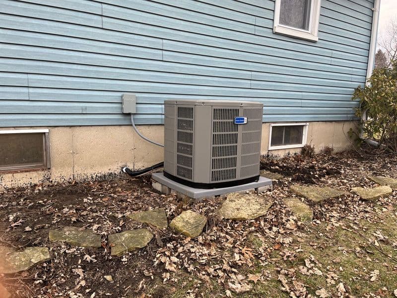Outdoor air conditioning unit installed beside a blue house, surrounded by landscaping.