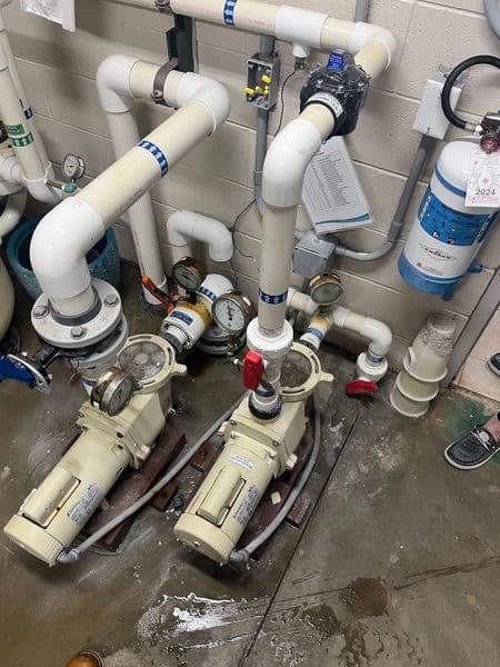 Two water pumps with connected pipes and gauges in a utility room.