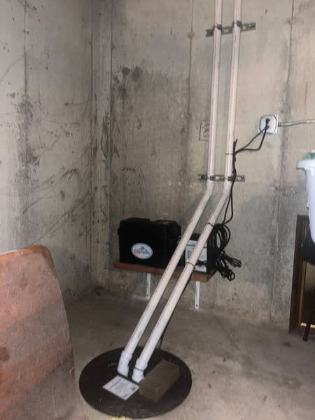 Sump pump installation in a basement with white pipes and electrical outlet.